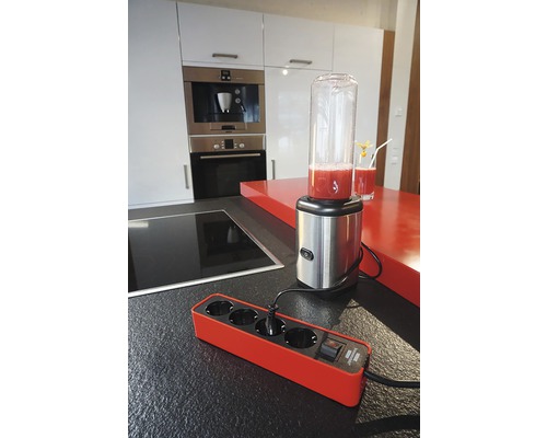 O bandă prelungitoare roșie cu patru prize și un mixer pe un blat de bucătărie.