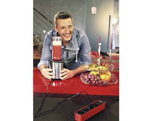 Un bărbat folosește un blender într-o bucătărie cu o bandă de alimentare și un bol cu fructe.