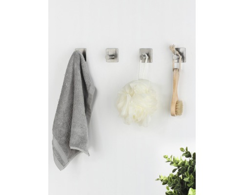 Trei cârlige de perete cu prosop, burete de duș și perie pe un perete