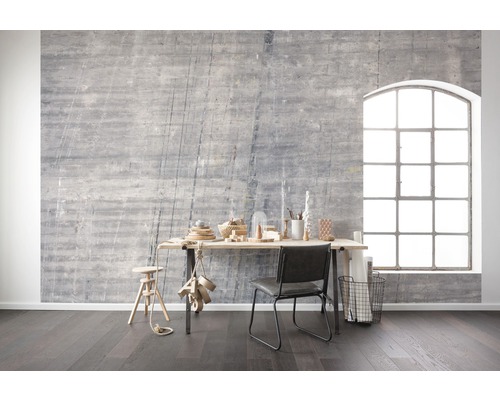 Cameră de zi cu perete de beton gri, birou, scaun și fereastră mare pentru o atmosferă luminoasă și modernă.