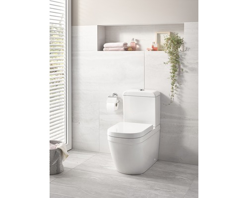 Toaletă albă pe podea într-o baie luminoasă cu raft de depozitare