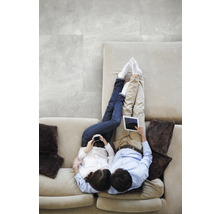 Un cuplu se relaxează pe o canapea cu tablete și telefoane mobile, cu gresie gri în fundal