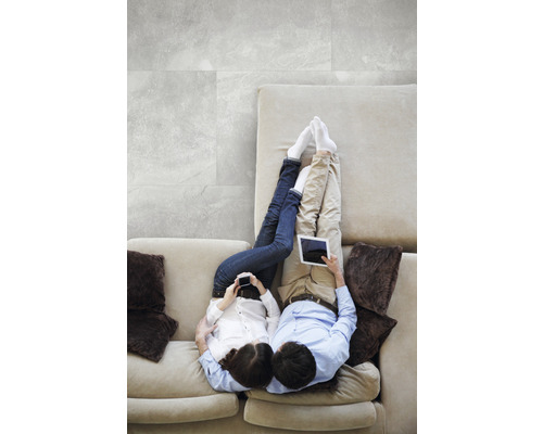 Un cuplu se relaxează pe o canapea cu tablete și telefoane mobile, cu gresie gri în fundal