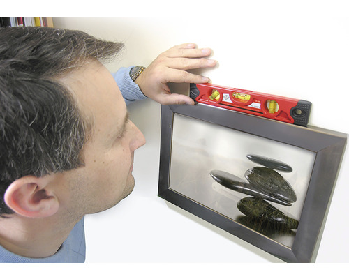 O persoană aliniază o imagine înrămată cu o nivelă.