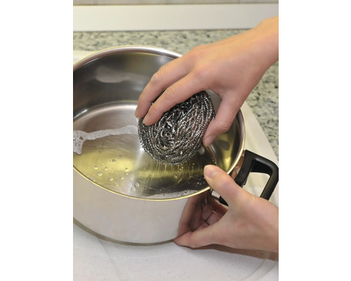 O persoană curăță o oală cu un burete de lână de oțel.