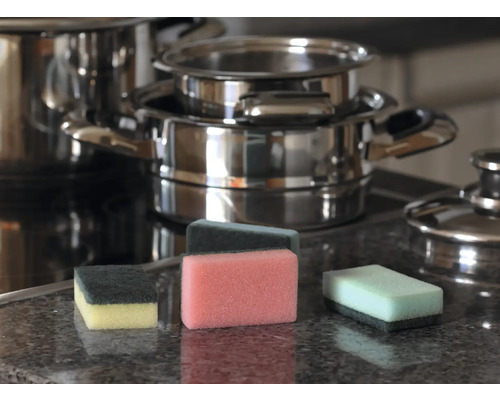 Mai mulți bureți de spălat vase pe un blat de bucătărie cu cratițe în fundal