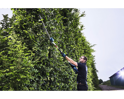 Un bărbat taie un gard viu cu o foarfecă de tuns gard viu cu acumulator