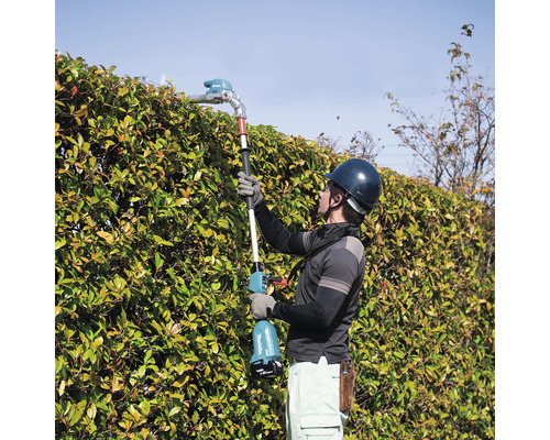Un bărbat care tunde un gard viu cu o foarfecă de gard viu fără fir.
