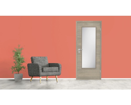 Living cu fotoliu tapițat gri, plantă de interior și ușă interioară cu inserție de sticlă.