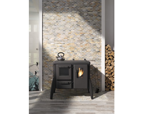 Fotografie de interior cu un aragaz, un ceainic, lemne de foc și un perete de cărămidă