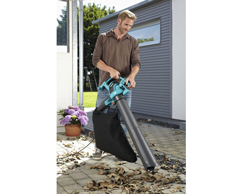 Un bărbat folosește un aspirator de frunze în grădină pentru a îndepărta frunzele.