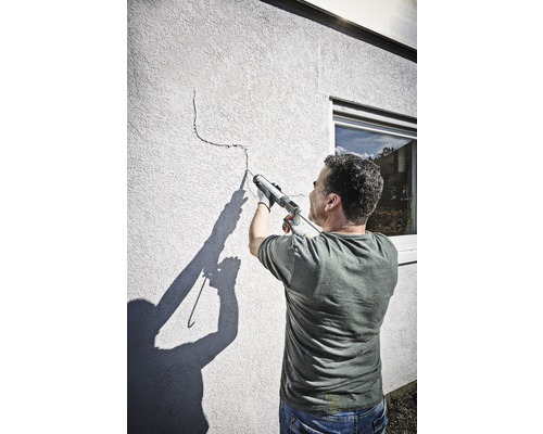 Un bărbat etanșează o fisură într-un perete cu un pistol de etanșare.