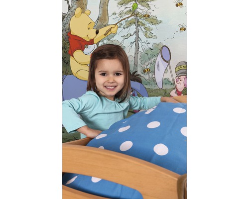 Fată în pat în fața unui tapet cu motivul Winnie the Pooh.
