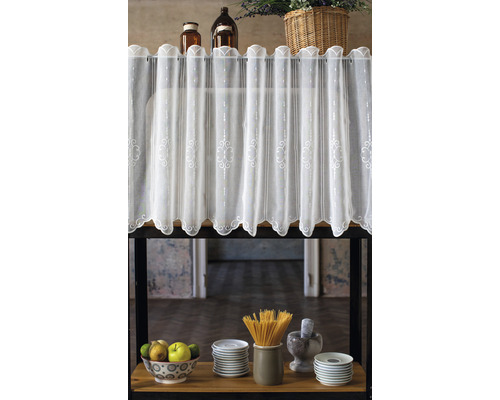 Perdea decorativă cu broderii deasupra unui raft cu ustensile de bucătărie.