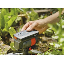 O mână operează un aspersor Gardena în grădină.