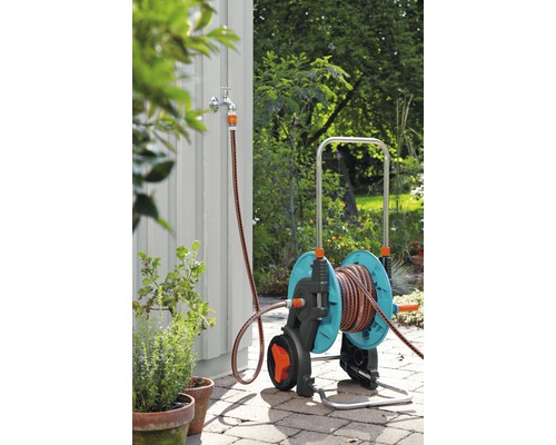 Scenă de grădină cu un cărucior pentru furtun de grădină cu racord de furtun la un robinet de apă