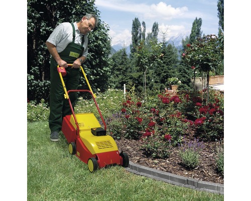 Un bărbat folosește o mașină de tuns iarba într-o grădină cu straturi de flori.