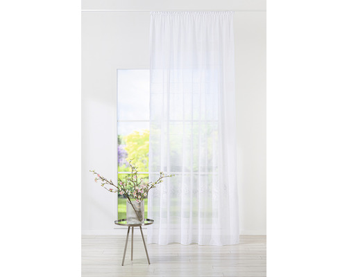 Perdea albă în fața unei ferestre cu vedere spre grădină și o masă cu o vază cu flori