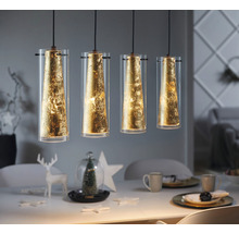 Lampa suspendată cu patru abajururi cilindrice din sticlă și decor cu foiță de aur deasupra unei mese de sufragerie.