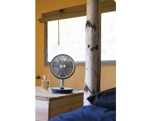 Ventilator de masă pe o masă de lemn lângă un pahar cu apă într-un cort.