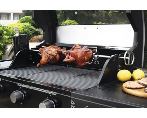 Grătar pe gaz cu doi pui fripți pe o frigăruie rotativă și lămâi pe o placă de lemn