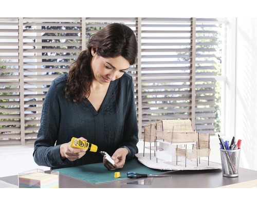 Femeie care construiește un model arhitectural cu adeziv pe un birou.