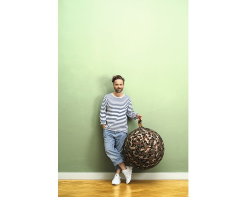 Un bărbat sprijinit de un zid ține în mână un sac de șezut rotund cu model de camuflaj