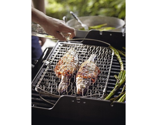 Doi pești și sparanghel verde pe un grătar cu o persoană care toarnă ulei deasupra