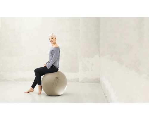 Femeie stând pe o minge de gimnastică într-o cameră luminoasă.