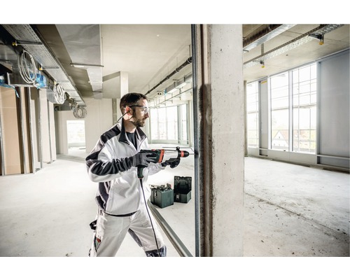 Un bărbat forează cu un ciocan rotopercutor o gaură într-un perete de beton într-o clădire în construcție