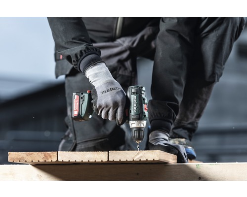 O persoană găurește o scândură de lemn cu o mașină de găurit cu acumulator.