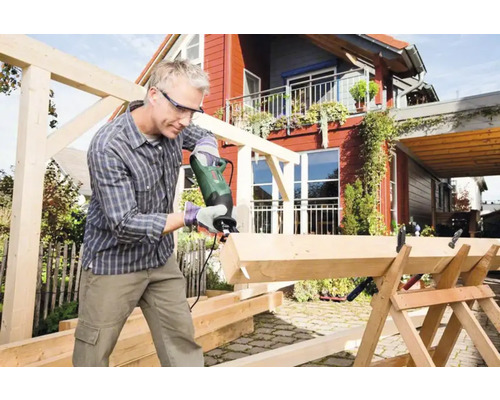 Bărbat taie lemn cu un ferăstrău electric în aer liber. Construcție din lemn în construcție.