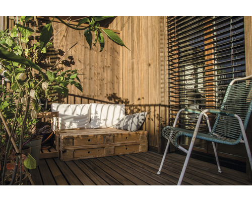 Balcon însorit cu terasă din lemn, palet ca loc de ședere, perne, scaun și plante