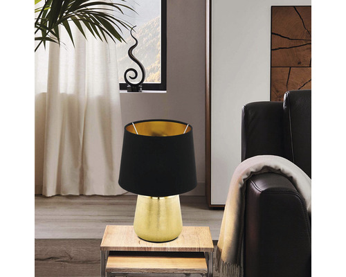 Lampă de masă decorativă cu abajur negru și bază aurie pe o măsuță laterală