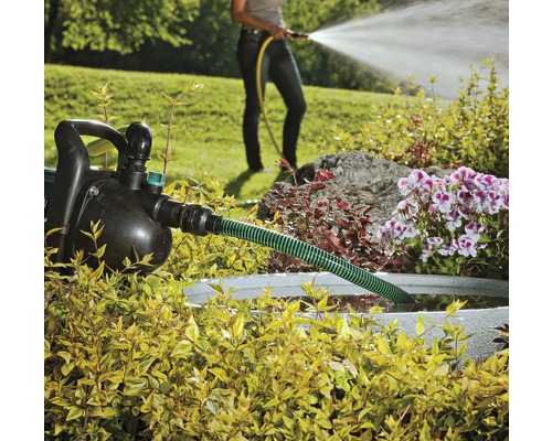 Grădină cu pompă de grădină, furtun și o persoană care udă cu un furtun de grădină