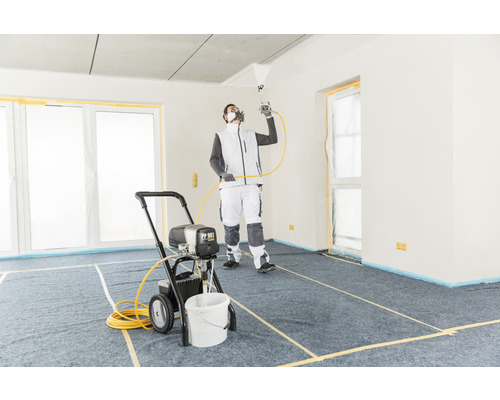 Un bărbat folosește un pulverizator de vopsea într-o încăpere acoperită pentru lucrări de vopsire.