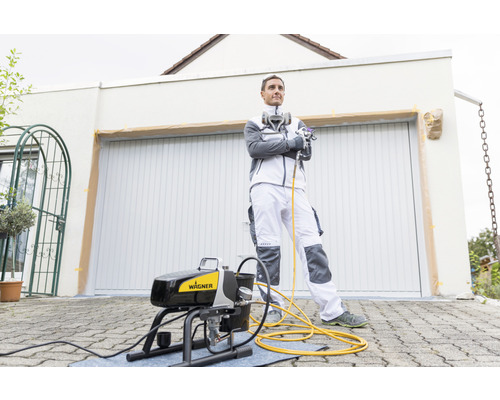 Bărbat cu pulverizator de vopsea Wagner în fața garajului