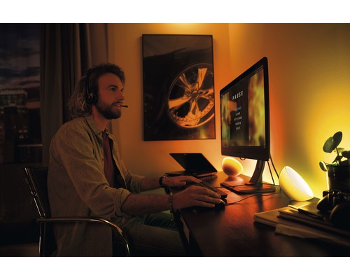 Scenă cu un bărbat cu căști în fața unui computer, luminat de două lămpi de masă