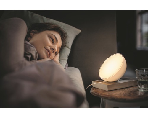 O femeie stă întinsă în pat lângă o lampă de noptieră.