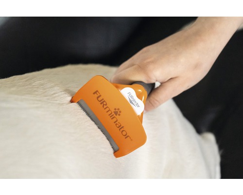 O mână folosește o perie de blană Furminator pe blana unui animal.