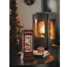 Glob decorativ cu zăpadă în formă de cabină telefonică cu motiv Moș Crăciun și șemineu în fundal.