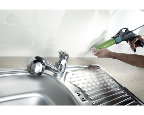 Un pistol de silicon etanșează o îmbinare deasupra unei chiuvete din oțel inoxidabil.