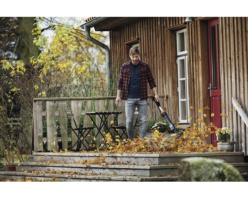 Un bărbat folosește o suflantă de frunze pe terasa de lemn a unei case