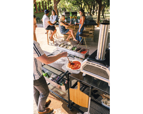 Scenă cu cuptor de pizza, ingrediente și persoane afară care fac pizza