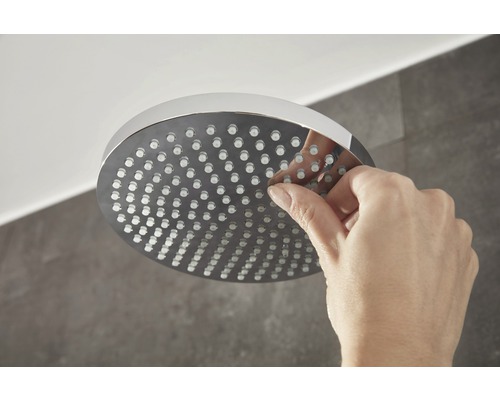 O mână curăță o pară de duș rotundă cu duze.