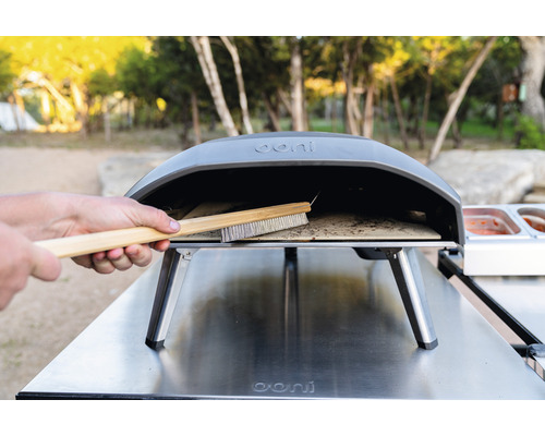 Logo Ooni. Curățarea unei perii de pizza într-un cuptor de pizza.