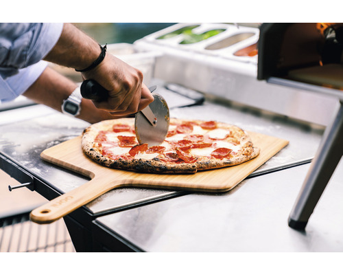 O pizza este tăiată pe o lopată de lemn cu un tăietor de pizza.
