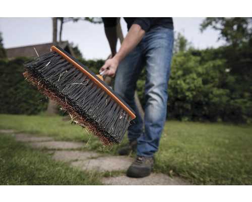 Persoană măturând gazonul cu o mătură de stradă