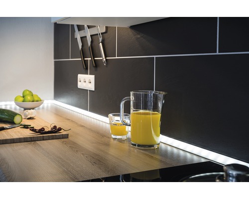 Scenă de bucătărie cu ulcior de suc, pahar, tocător și ustensile de bucătărie în fața unui fundal de faianță neagră