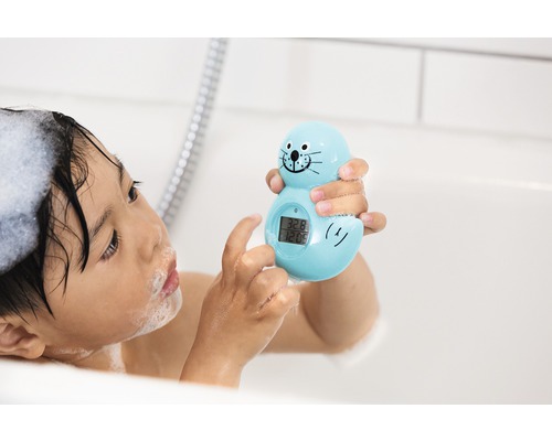 Un copil în baie ține un termometru de baie în formă de focă.